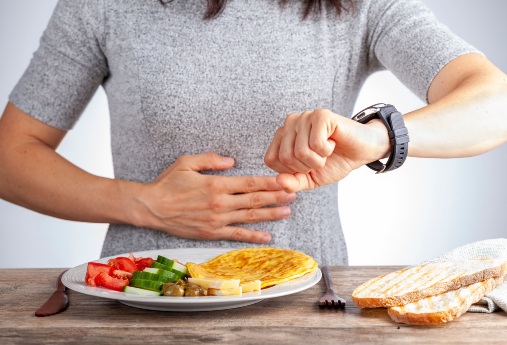 Woman checking smartwatch next to plate of food, representing OMAD intermittent fasting timing