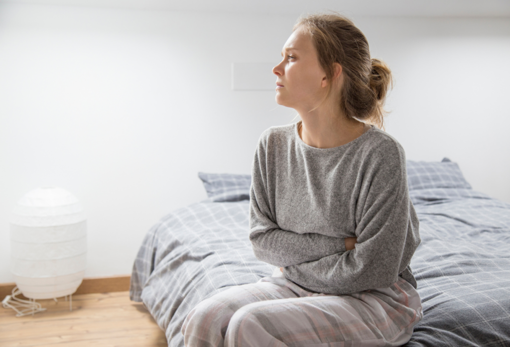midlife woman sitting on bed looking worried and burned out