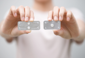 Hands comparing two hormone therapy pill packs, representing different hormone replacement therapy options for women in menopause.